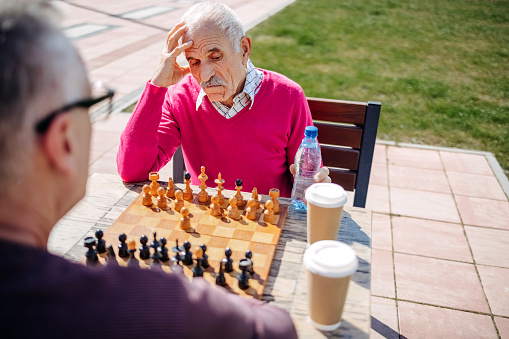 Senior adult making starting move in chess game wearing pink sweater in city park