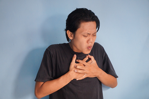 Asian young man in black t-shirt with chest pain expression.