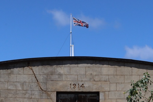 Union Jack flying on a flagpole with an abandoned water tank building in the foreground on the tropical British Overseas Territory of Ascension Island