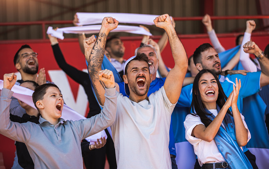 Football or soccer fans are cheering for their team at the stadium on the match