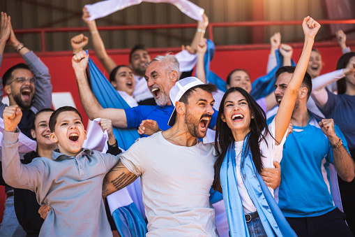 Football or soccer fans are cheering for their team at the stadium on the match