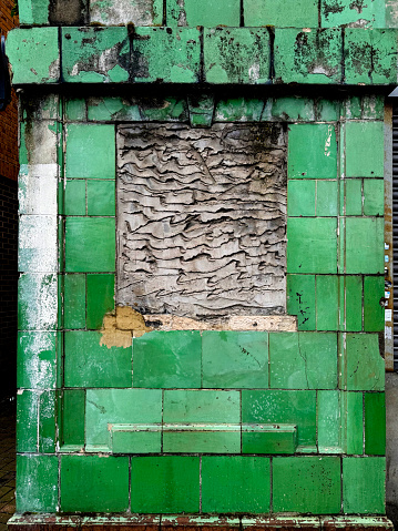 A window in a green tiled wall in a derelict old pub blocked with concrete