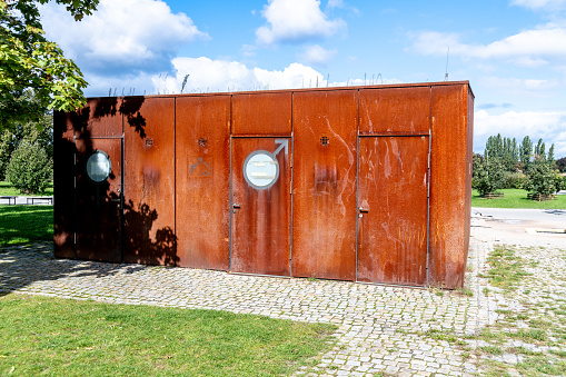 A weathered public restroom stands amidst the greenery of a Prague park