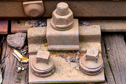 Macro detail of rail fasteners, rusted bolts, and nuts on weathered wooden railway ties
