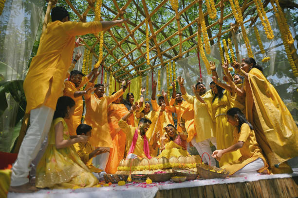 Family and friends showering floral blessings on bride and groom during haldi ceremony Family and friends dressed beautifully in a yellow attire gather around the bride and groom during their haldi ceremony, dancing joyously to the lively beats. With laughter echoing and hands clapping, they create a circle of love, warmth and support. Each step is a testament to the shared happiness, marking the beginning of a new journey filled with love, laughter, and cherished memories haldi ceremony stock pictures, royalty-free photos & images