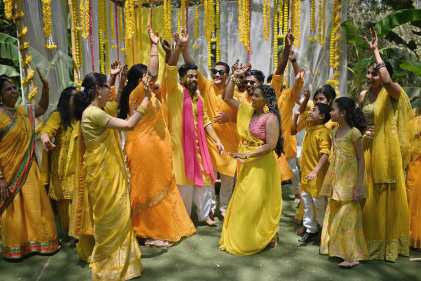 Family and friends dance with bride and groom during their haldi ceremony Family and friends join the bride and groom to dance during their haldi ceremony. Dressed in vibrant hues of yellow, they sway to the rhythmic beats, filling the air with laughter and joy. Amidst the colorful festivities, the dance becomes a vibrant tapestry of love, marking the beginning of a new chapter filled with happiness and camaraderie haldi ceremony stock pictures, royalty-free photos & images