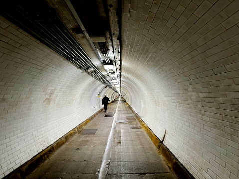 An adult man walking through Woolwich Foot Tunnel, an old Victorian tunnel under the Thames. Woolwich, London, April 2024
