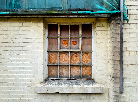 A window in the basement of an old brick building and a concrete staircase.