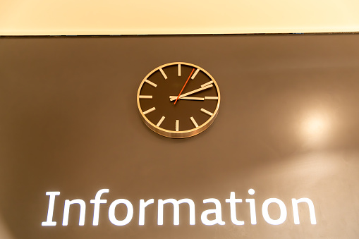 Bautzen, Saxony - Germany - 04-10-2021: Modern wall clock above 'Information' sign in high contrast on a dark wall