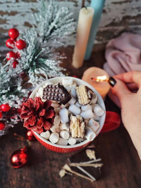 istock Cup of christmas hot cocoa with marshmallows and cinnamon on a table with christmas tree pine candles 2127682244