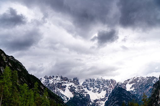 Alpen, South Tyrol - Italy - 06-07-2021: Close-up of dark clouds looming over partly snow-covered mountain peaks in the Alps, creating a dramatic scene