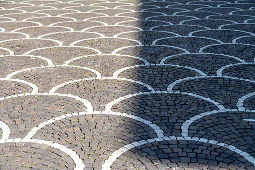 Treviso, Venetien - Italy - 06-08-2021: Attractive geometric cobblestones with interwoven arches of gray and white paving stones that are half in the sunlight and half in the shade
