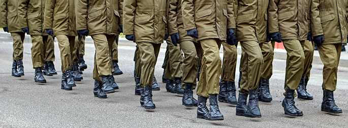 Disciplined soldiers in camouflage march in perfect synchronization during a military parade. Helmets and rifles add to the display of unity and strength, evoking pride.