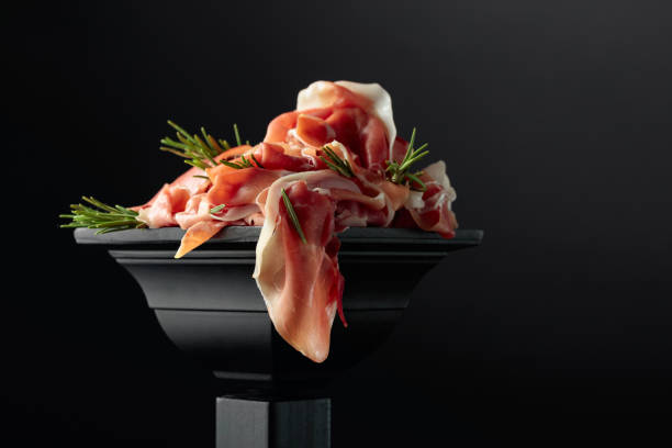 Prosciutto with rosemary on a black podium.