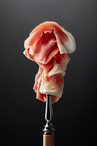 Thin slices of prosciutto on a fork.