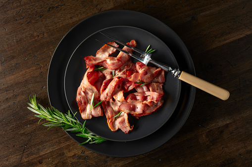 Roasted bacon slices with rosemary on an  old wooden table. Copy space. Top view.