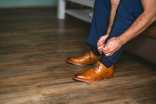 Man dressing up with elegant leather shoes. Groom preparing for wedding ceremony at wedding day. Man getting ready for work, blue trousers