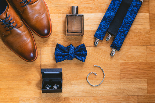 Groom's accessories, spread out on the wooden floor. Shoes, perfume, bow tie, shoulder straps, cufflinks and bracelet