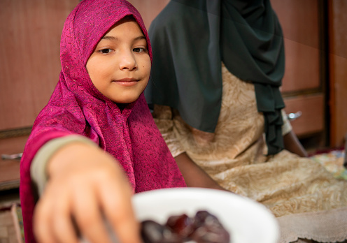 Two happy Islamic girls in hijab eating traditional dates fruits during Ramadan fasting month at home.