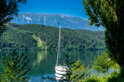 Millstatt am See, KÃ¤rnten - Austria - 06-16-2021: MillstÃ¤tter Lake: An anchored sailboat floats on a tranquil Austrian lake, framed by alpine mountains and trees