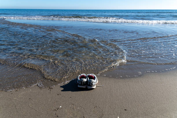 Cabo de Gata, Almeria - Spain - 01-23-2024: A pair of sneakers left on a sandy beach as gentle waves caress the shore