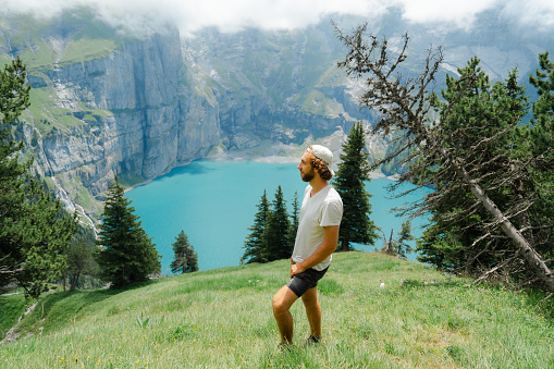 Cheerful man hiking near Oeschinensee lake in Swiss Alps in summer  and enjoying pristine nature