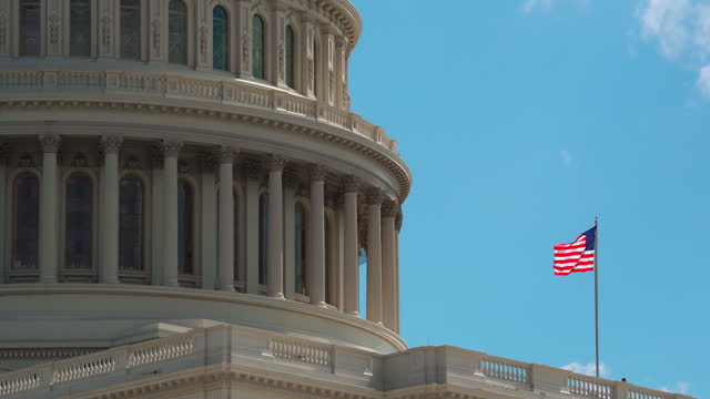 The United States Capitol Building and USA flag with blue sky and cloudscape in Washington, D.C., United States