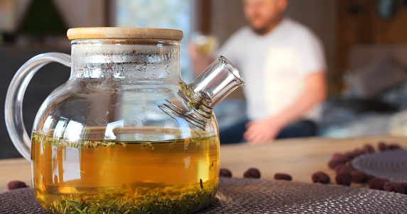 Man walks away from glass teapot with freshly brewed tea, holding mug, to enjoy flavor of Chinese oolong tea. Embrace essence of traditional Chinese tea. Traditional chinese tea concept.