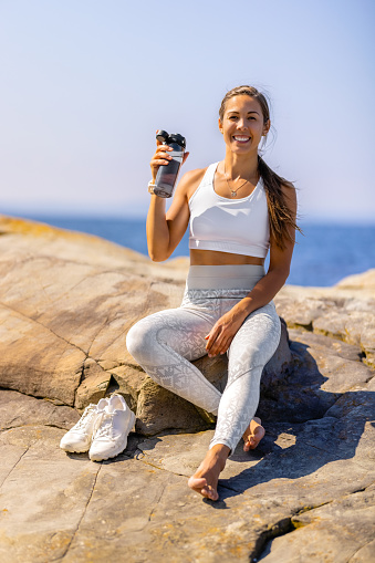 Portrait of smiling female athlete with water bottle resting on rock during sunny day