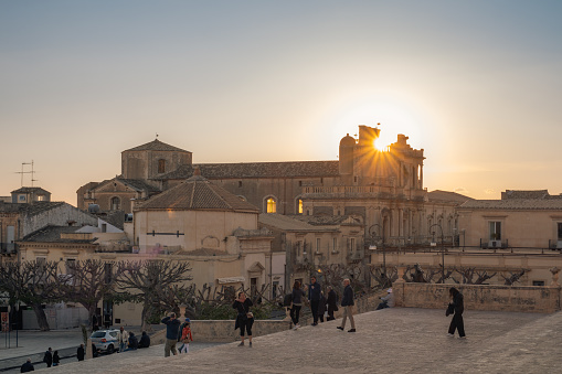 03-23-2024; Noto, Syracuse, Sicily, Italy: Sunset on the baroque town of Noto from the staircase of the Cathedral of Saint Nicolò. Some occasional people (could be tourists) walking on a staircase.