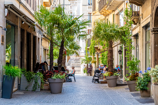 Vicenza, Venetien - Italy - 06-12-2021: People enjoy their time in cafes on an alley lined with palm trees and decorated with flowering plants in Vicenza, Italy, amidst historic architecture