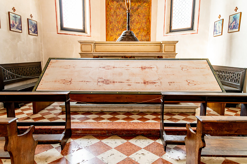 Vicenza, Venetien - Italy - 06-12-2021: Chapel interior with a framed replica of the Shroud of Turin on display, flanked by pews and religious artwork in Vicenza