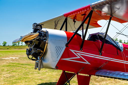 Caorle, Venetien - Italy - 06-14-2021: Front half of a red two-seater biplane with red-silver wings on a green field in Italy