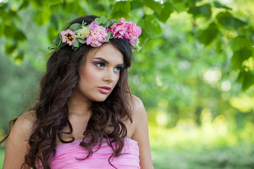 Stylish healthy woman with makeup and long wavy dark brown hairstyle with flowers on head in spring park outdoor