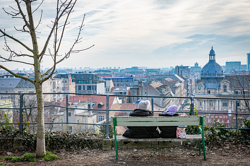 February 3rd, 2024. Zagreb. Two persons on a park bench admiring the view of the skyline and rooftops of the city.