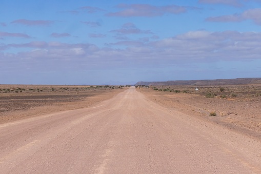Panoramic picture over a gravel road through the desert like steppe in southern Namibia under a blue sky in summer