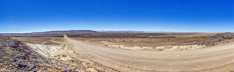 Panoramic picture over a gravel road through the desert like steppe in southern Namibia under a blue sky in summer