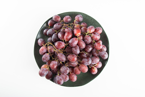 Plate with purple grapes and white background.