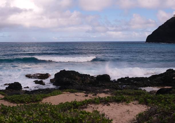 Makapuu Beach on Oahu and the coastline.  Rabbit Island off the coast of Oahu surrounded by the blue Pacific Ocean and the horizon over water.  Waves rolling onto shore and crashing onto the lava rocks along the coast.
