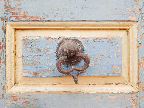 Close up of Rusted iron ring handle on peeling and eaten old wooden door. Construction and architectural details.