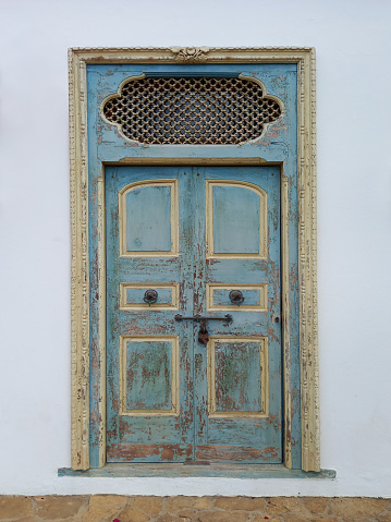 Close-up of broken and uncorked wooden door entrance with round door knobs. Old door with rusty and spoiled paint.