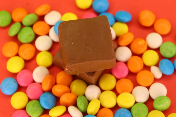 A vibrant assortment of candies spills from an overturned bowl, creating a colorful pattern on a dark background. The candies display various bright colors.