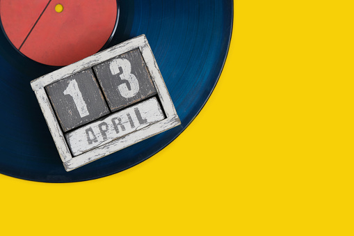 April 13 on calendar lying on a vinyl record on yellow background. World Rockenroll Day.