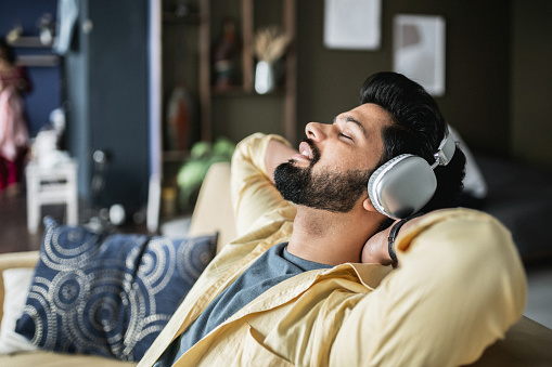 Moment of relaxation and mind calmness. Young Indian man listens to music in living room