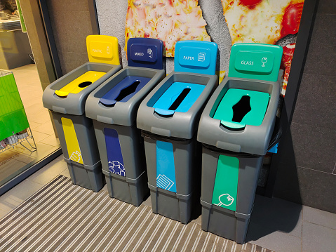 Several multi-colored plastic containers stand for separate garbage collection with appropriate inscriptions and emblems