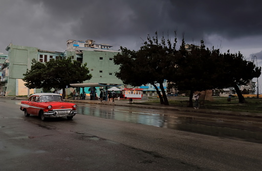 Havana, Cuba-October 8, 2019: Red-white old American classic car -almendron, yank tank- Pontiac Chieftain 4-door Sedan 1957 drives down San Lazaro Street past Antonio Maceo Park after a heavy downpour