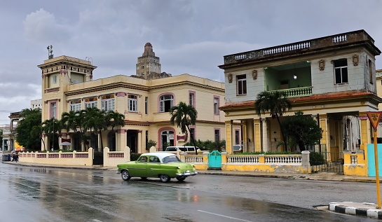 Havana, Cuba-October 8, 2019: Green-white American classic car -almendron- Ford Customline 4-door Sedan 1953 drives down Calle 15 Street to intersect with Linea Street, wet after heavy afternoon rain.