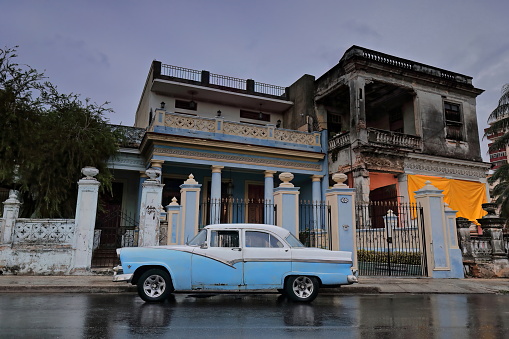 Havana, Cuba-October 8, 2019: Blue-white American classic car -almendron- Ford Fairlane 4-door Sedan 1955 with 1956 model's steel side-stripe stationed on Linea Street, wet after heavy afternoon rain.