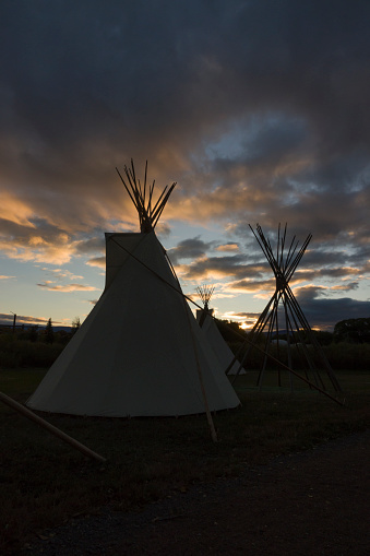 At sunrise, a pair of silhouetted teepees or tipis stand on the grassy grounds of the Ute Indian Museum in Montrose Colorado.