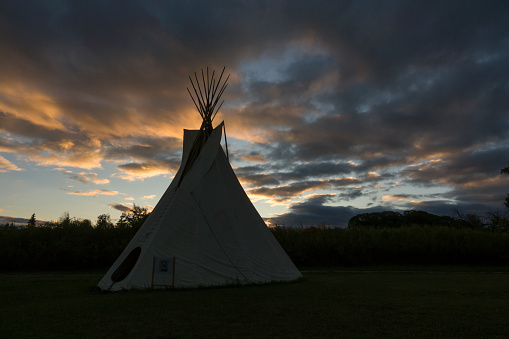 Three teepees (also called tipis or tepees) which are Native American tents, stand on a grassy hill in the plains of the American west. 3D Rendering
